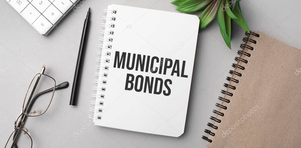 MUNICIPAL BONDS is written in a white notebook with calculator, craft colored notepad, plant, black marker and glasses.