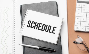 Not defterinde program ve kahverengi arka planda çeşitli iş kağıtları. Kahverengi gözlükler ve not defteriyle büyüteç.