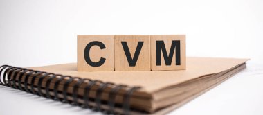 Text CVM on the wooden cubes and craft colored notepad on the white background