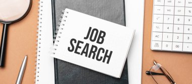 JOB SEARCH on notepad and various business papers on brown background. Brown glasses and magnifier with notepad.