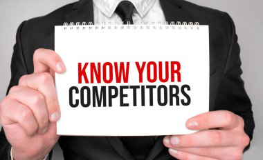 Businessman holding a notepad with text KNOW YOUR COMPETITORS