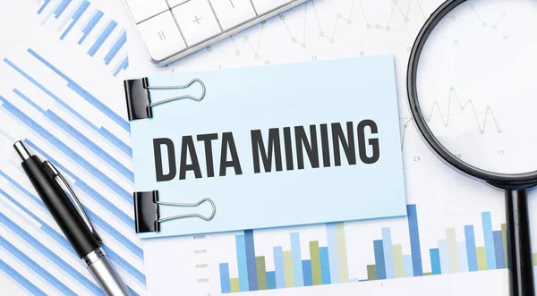 Top view of text DATA MINING with calculator, magnifying glass and pen on financial charts . Business, calculation, strategy, searching and tax concept. Top view.