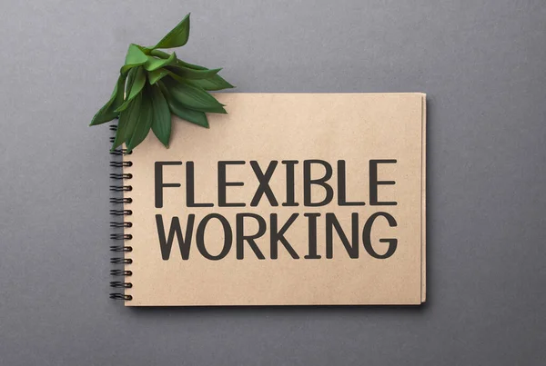 FLEXIBLE WORKING text on craft colored notepad and green plant on the dark background