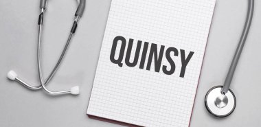 Bej bir arka planda, steteskop ve üzerinde quinsy yazan beyaz bir not defteri. Tıbbi konsept