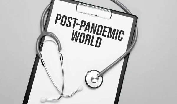 The words post-pandemic world is written on white paper on a grey background near a stethoscope. Medical concept