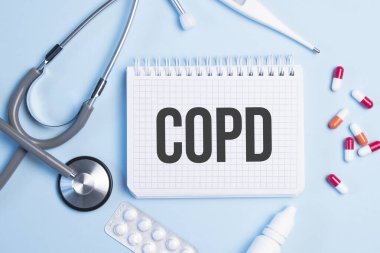 Copd kelimesi beyaz bir not defterine steteskop, şırınga, elektronik termometre ve hapların yanında mavi bir arkaplan üzerine yazılmış. Tıbbi konsept