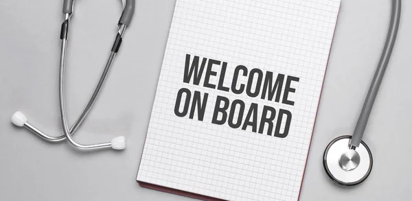 On a beige background, a stethoscope and a white notepad with the inscription welcome on board. Medical concept