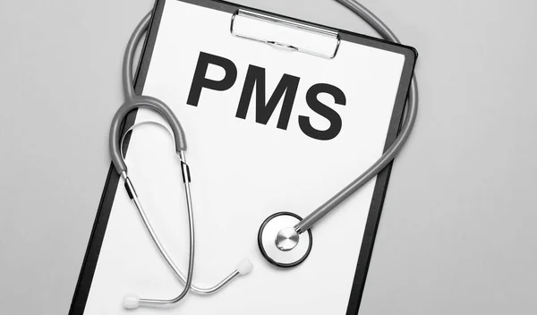 The words pms, is written on white paper on a grey background near a stethoscope. Medical concept
