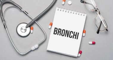 Defterde bronş yazı var, steteskop, hap ve gözlüğün yanında..