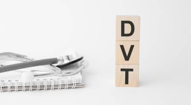 Beyaz arka planda izole edilmiş tahta küplere dvt yazıtları, tıp konsepti. Masanın yanında steteskop ve haplar var..