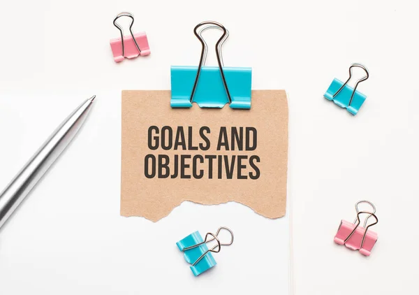 İş ve finans kavramı. Beyaz bir arka planda bir defter, bir kalem, mandallar ve karton bulunur - Hedefler ve Hedefler