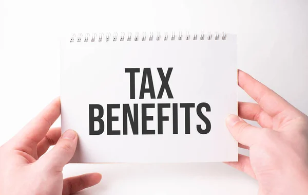TAX BENEFITS word inscription on white card paper sheet in hands of a man. Black letters on white paper. Business concept.