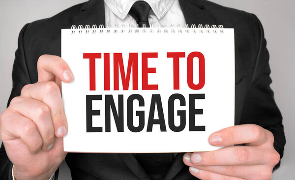 Бизнесмен держит в руках блокнот с текстом Time To Engage