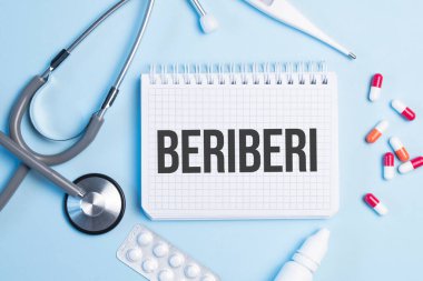 Beriberi kelimesi, steteskop, şırınga, elektronik termometre ve hapların yanındaki mavi arka planda beyaz bir not defterine yazılmıştı. Tıbbi konsept