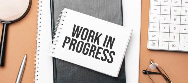 Not defteri üzerinde çalışma devam ediyor ve kahverengi arka planda çeşitli iş belgeleri var. Kahverengi gözlükler ve not defteriyle büyüteç.