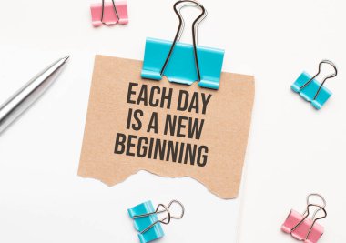 İş ve finans kavramı. Beyaz bir arka planda bir defter, bir kalem, mandallar ve kartonda her gün yeni bir başlangıç var.