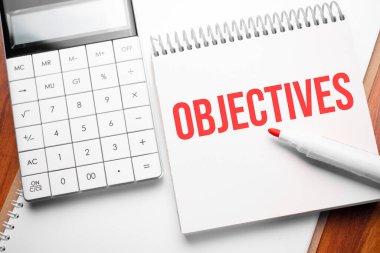 Hesap makinesi ve kırmızı işaretli tahta arkaplan üzerinde OBJECTIVES metin ile not