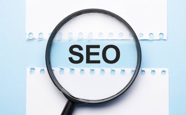 Mavi masadaki iki kağıdın arasında işaret dilimi olan büyüteç..