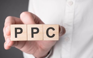 İş adamı elinde ppc metni olan tahta bir küp tutuyor. Mali, pazarlama ve iş kavramları