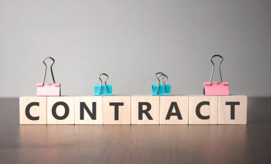 El, imza kontratıyla birlikte tahta bir küp koyuyor. Kelime, gri arka plandaki karanlık masanın üzerinde duran tahta küplere yazılmıştır..