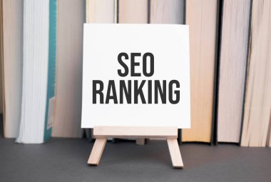 Metin seo sıralamasına sahip beyaz kart, dizilmiş kitapların arka planına karşı masanın üzerinde duruyor