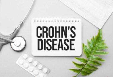 Crohn's disease word on notebook,stethoscope and green plant clipart