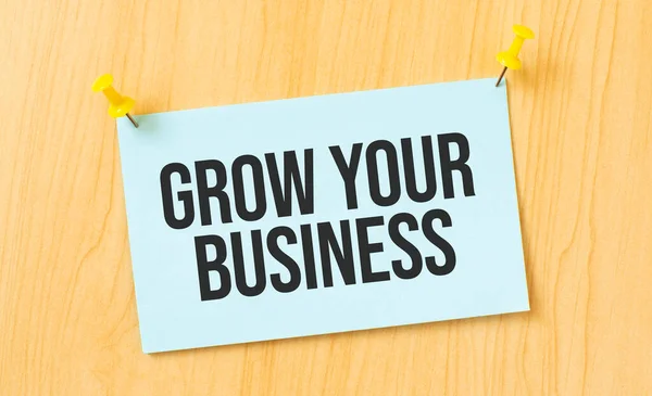 GROW YOUR BUSINESS sign written on sticky note pinned on wooden wall