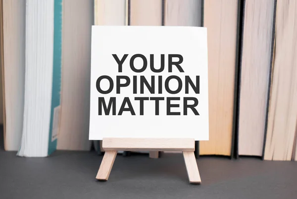 White card with text Your Opinion Matter stands on the desk against the background of books stacked