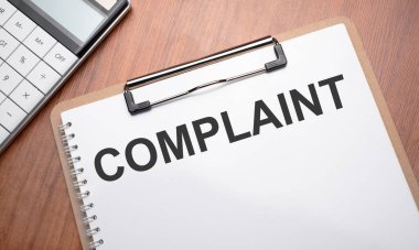 Tahta arkaplan, ataç, kalem ve hesap makinesiyle ilgili metin şikayeti içeren not defteri