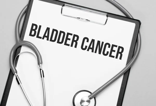 The words Bladder Cancer is written on white paper on a grey background near a stethoscope. Medical concept