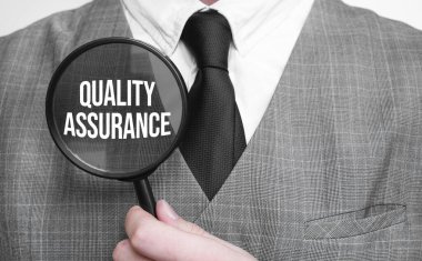 Kalite Güvencesi. Eğitim konsepti. İş adamı elleri büyüteçle.