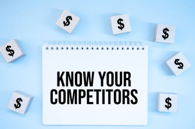 Dolar sembollü ahşap küpler, üzerinde yazı olan bir kağıt parçası ortada duran ahşap bir masa üzerindeki COMPETITORS biliyorum