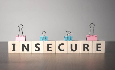 El, emniyetsiz işaretli tahta bir küp koyuyor. Kelime, gri arka plandaki karanlık masanın üzerinde duran tahta küplere yazılmıştır..