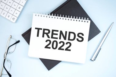 Metin 2022 eğilimlerini gösteriyor. Gri arkaplanda hesap makinesi, kalem, plan, gözlük ve siyah klasör