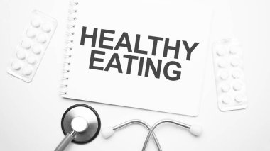 Metni yazmak için tablet üzerinde sağlıklı beslenme, steteskop ve beyaz tabletlerin yanında.