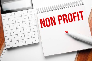 Hesap makinesi ve kırmızı işaretleyici ile tahta arkaplan üzerinde Non Profit metin ile not