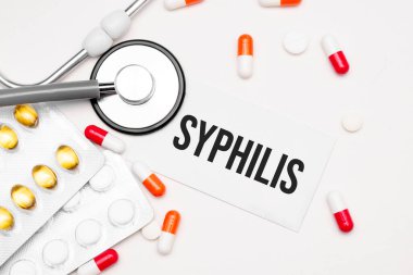 Stethoscope, pills and notebook with Syphilis word on medical desk.