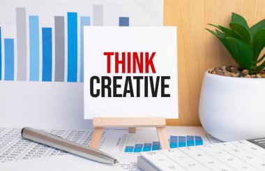 text Think Creative on easel with office tools and paper.Top view.