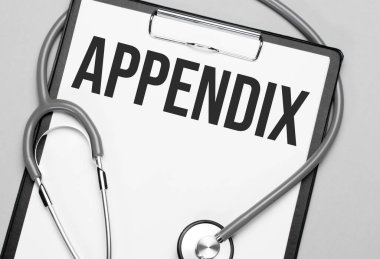 APPENDIX kelimeleri beyaz kağıda steteskopun yanındaki gri bir arka planda yazılır. Tıbbi konsept
