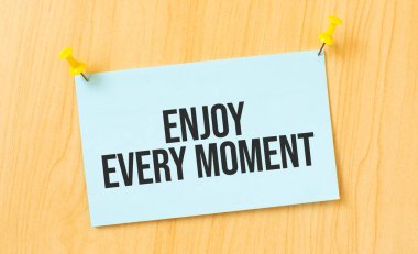 Tahta duvara yapıştırılmış yapışkan nota yazılmış her anın tadını çıkar.