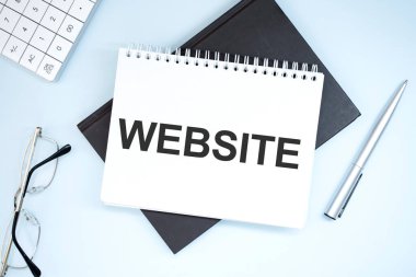 Web sitesi yazılıyor. Gri arkaplanda hesap makinesi, kalem, plan, gözlük ve siyah klasör