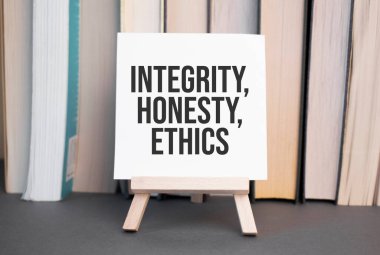 Yazılı beyaz kart, TEGRİSTİ, ETHICS, masadaki kitapların arka planında duruyor