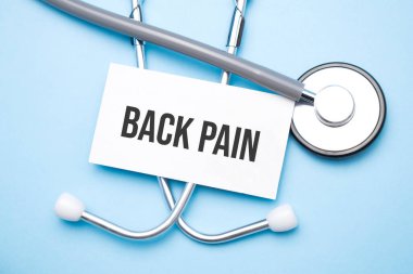 Stetoskop, tıbbi masanın üzerinde sırt ağrısı metni olan kağıt..