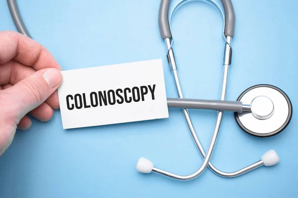 the doctor's hands holds a business card with the text of Colonoscopy with one hand and the other points to the text.