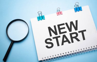 Mavi masadaki kağıt not defterinde yeni bir başlangıç işareti olan büyüteç silindiri.