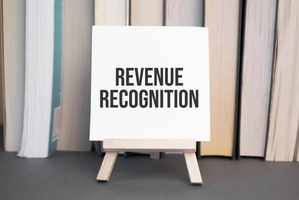 White card with text revenue recognition stands on the desk against the background of books stacked