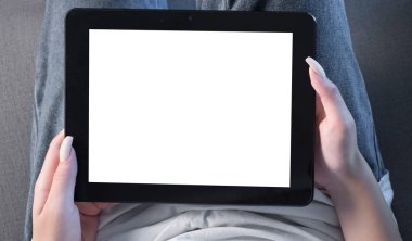 Genç kadın evinde kanepede kahve içerken tablet kullanıyor.