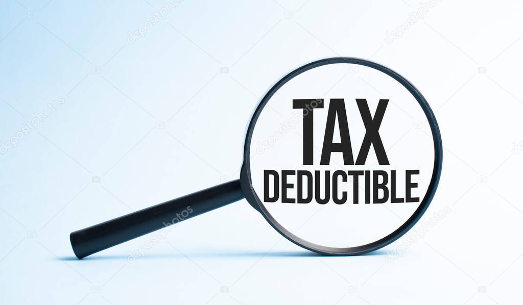 Magnifying glass with the word TAX DEDUCTIBLE. Business concept