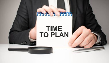 Adam gümüş bir kalem ve el ele tutuşma kartıyla Time to Plan diye bir not defteri yazmış. Gri arka plan, ön manzara. işletme ve eğitim kavramı.