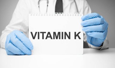 Doktorun elinde steteskopla K vitamini yazılı beyaz etiket.